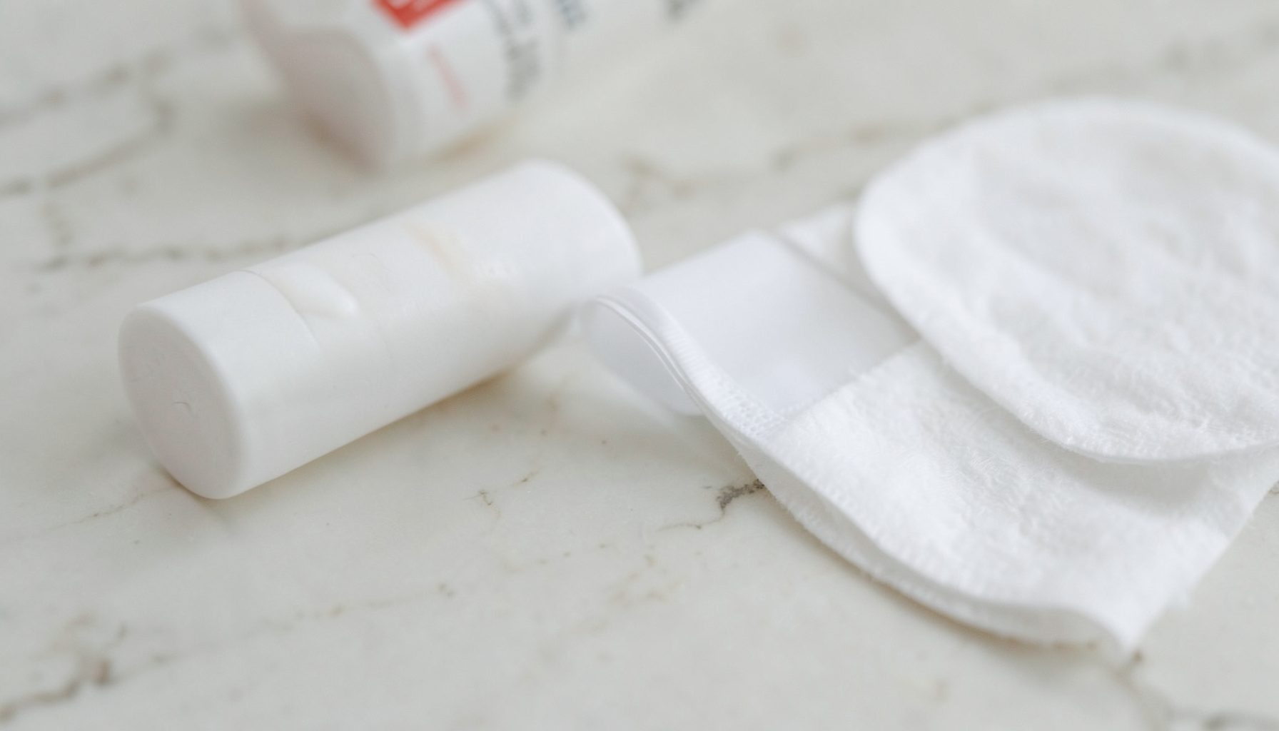 close-up of a spot treatment tube and cotton pads on a pale marble surface, clinical yet soft mood