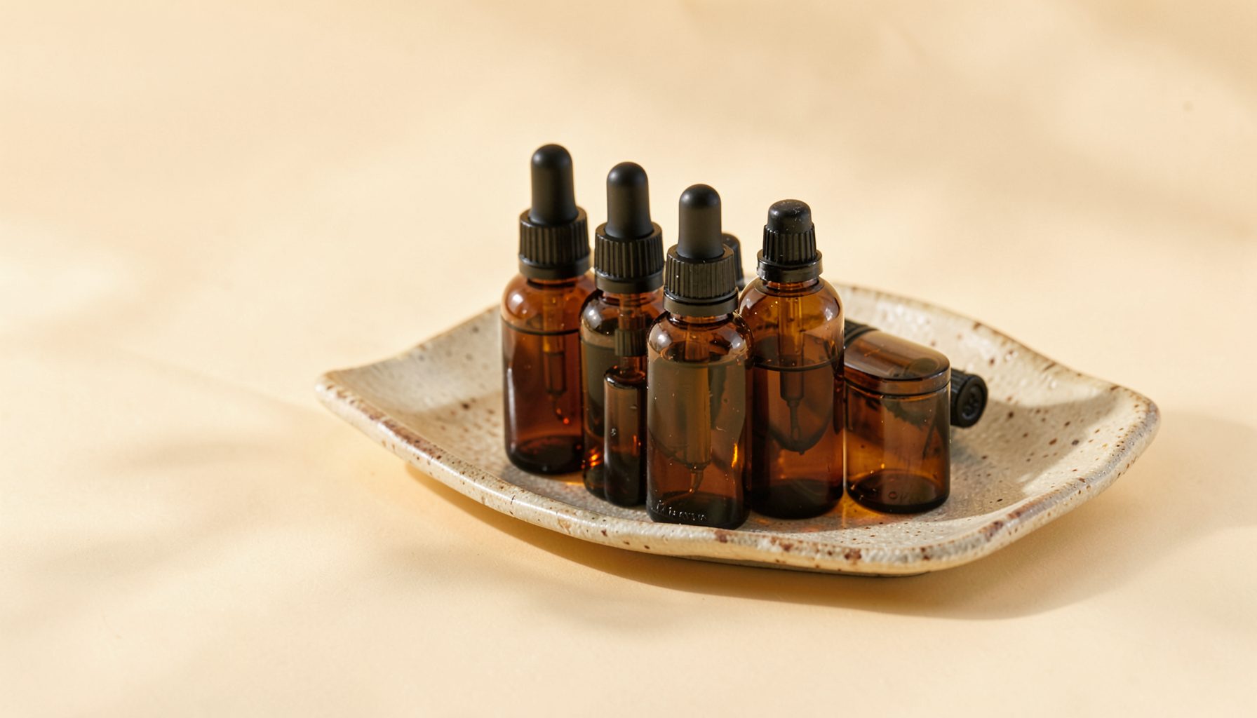 A cluster of amber glass dropper bottles and a textured ceramic dish on a warm cream background