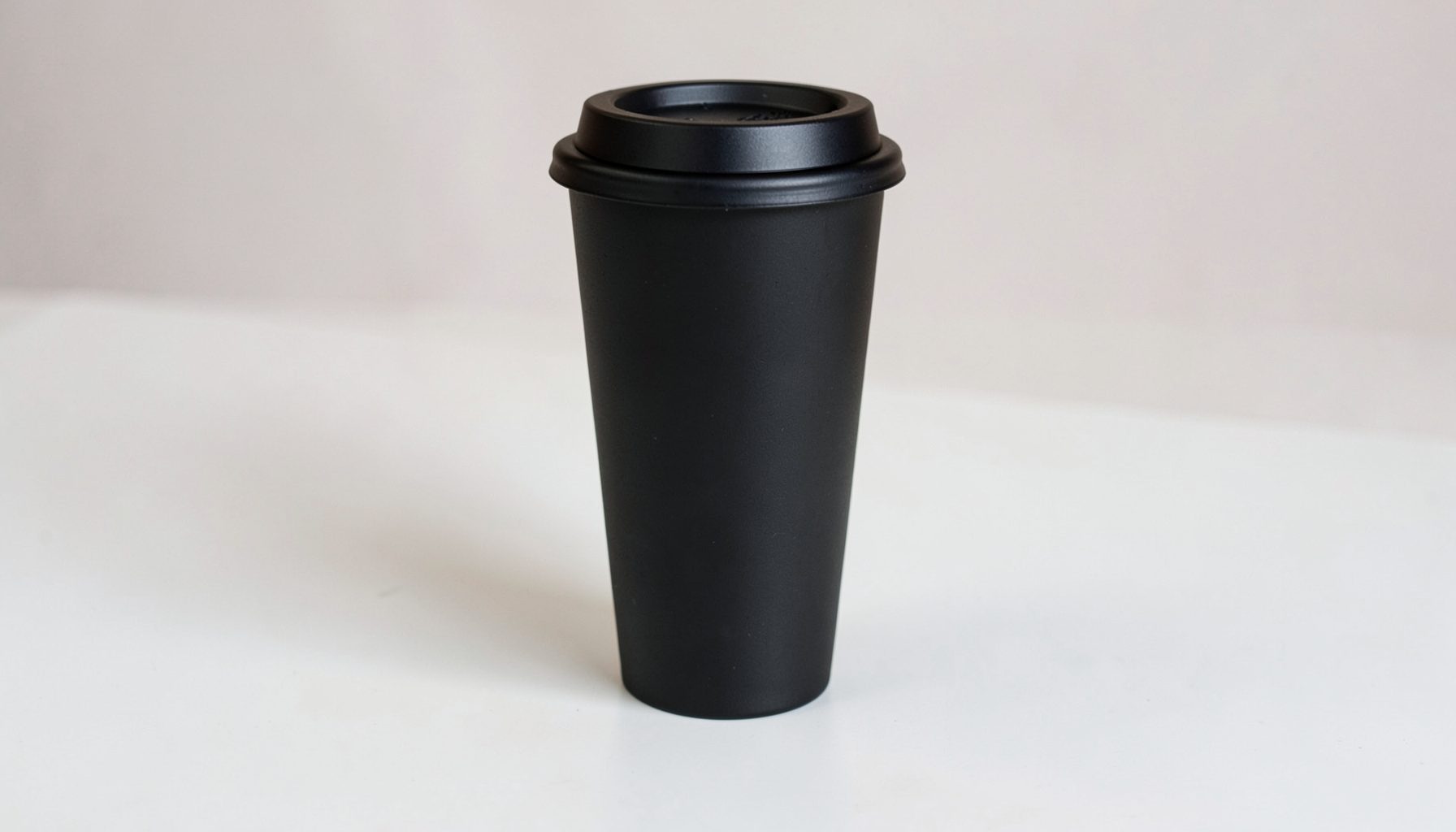 A matte black reusable coffee cup with a minimalist design on a light table