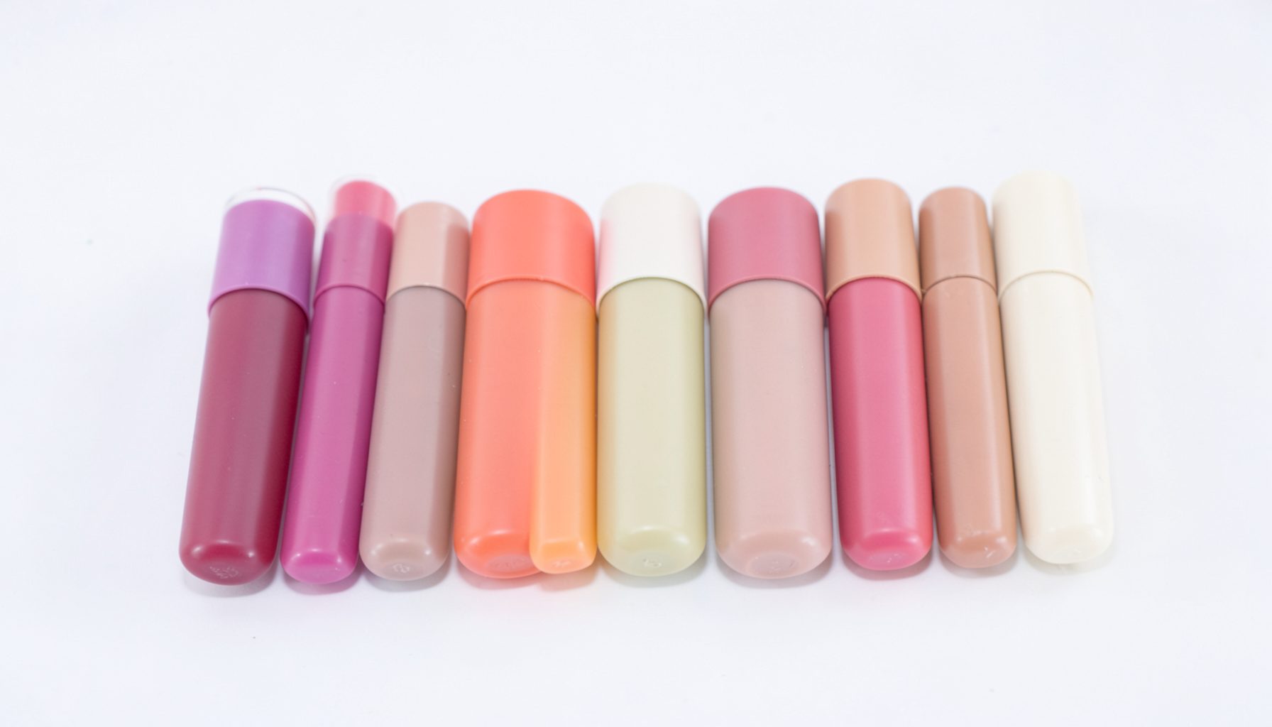 A row of tinted lip balm tubes in soft berry and nude shades on a clean white surface